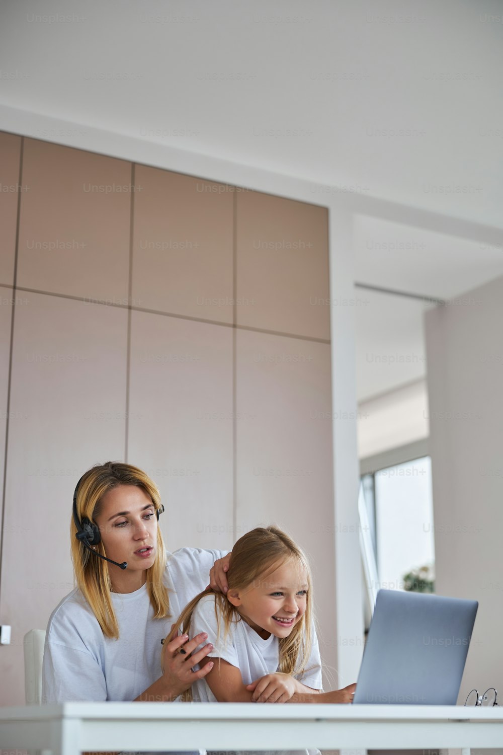 Side view portrait of adult charming mother spending time with little daughter while watching something on screen laptop in living room