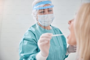 フェイスシールドを着けた専門の検査技師が、綿棒を女性患者の喉に挿入します。
