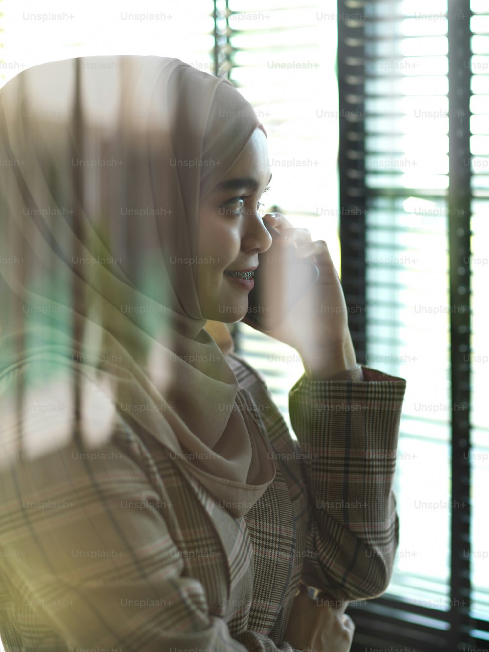 オフィスの部屋で電話で話している若いイスラム教徒のビジネスウーマンのガラスの壁越しの眺め