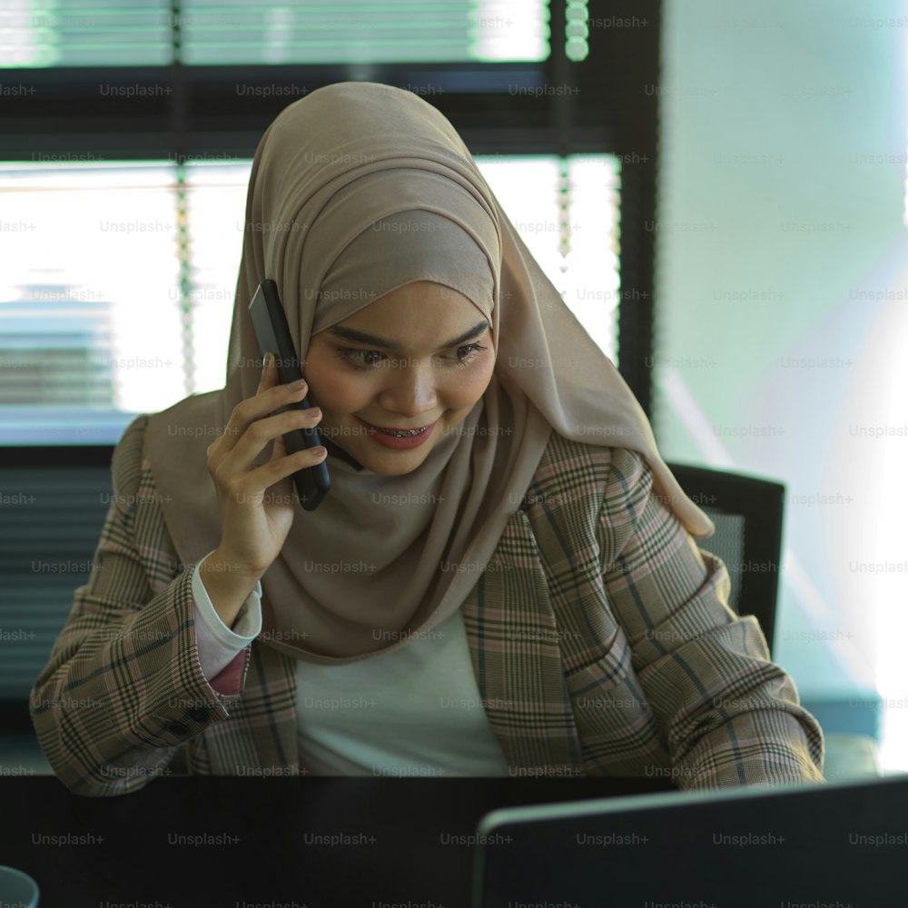 Retrato de una joven mujer de negocios musulmana hablando por teléfono mientras trabaja en la oficina