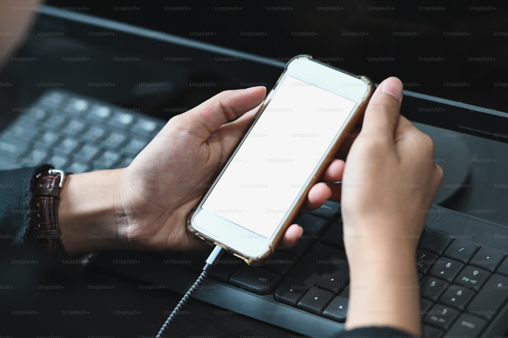 Vista de cerca de manos femeninas sosteniendo la pantalla en blanco del teléfono inteligente en el espacio de trabajo.