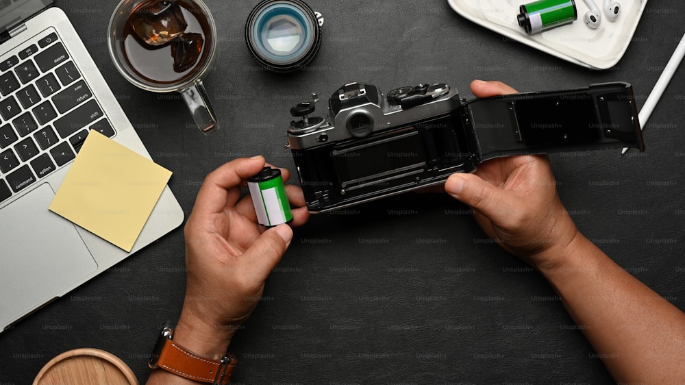 Vue de dessus des mains masculines utilisant un appareil photo argentique sur une table noire avec des fournitures et des accessoires