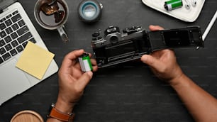 Top view of male hands using film camera on black table with supplies and accessories