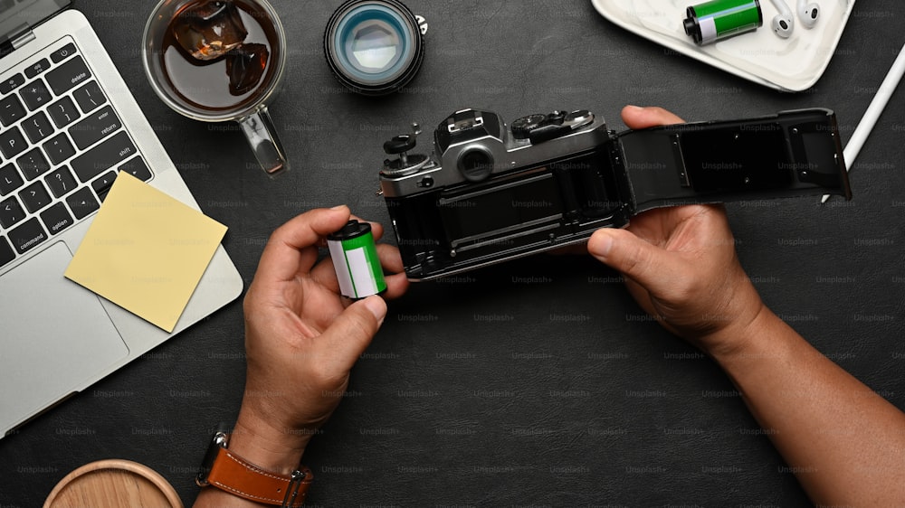 Top view of male hands using film camera on black table with supplies and accessories