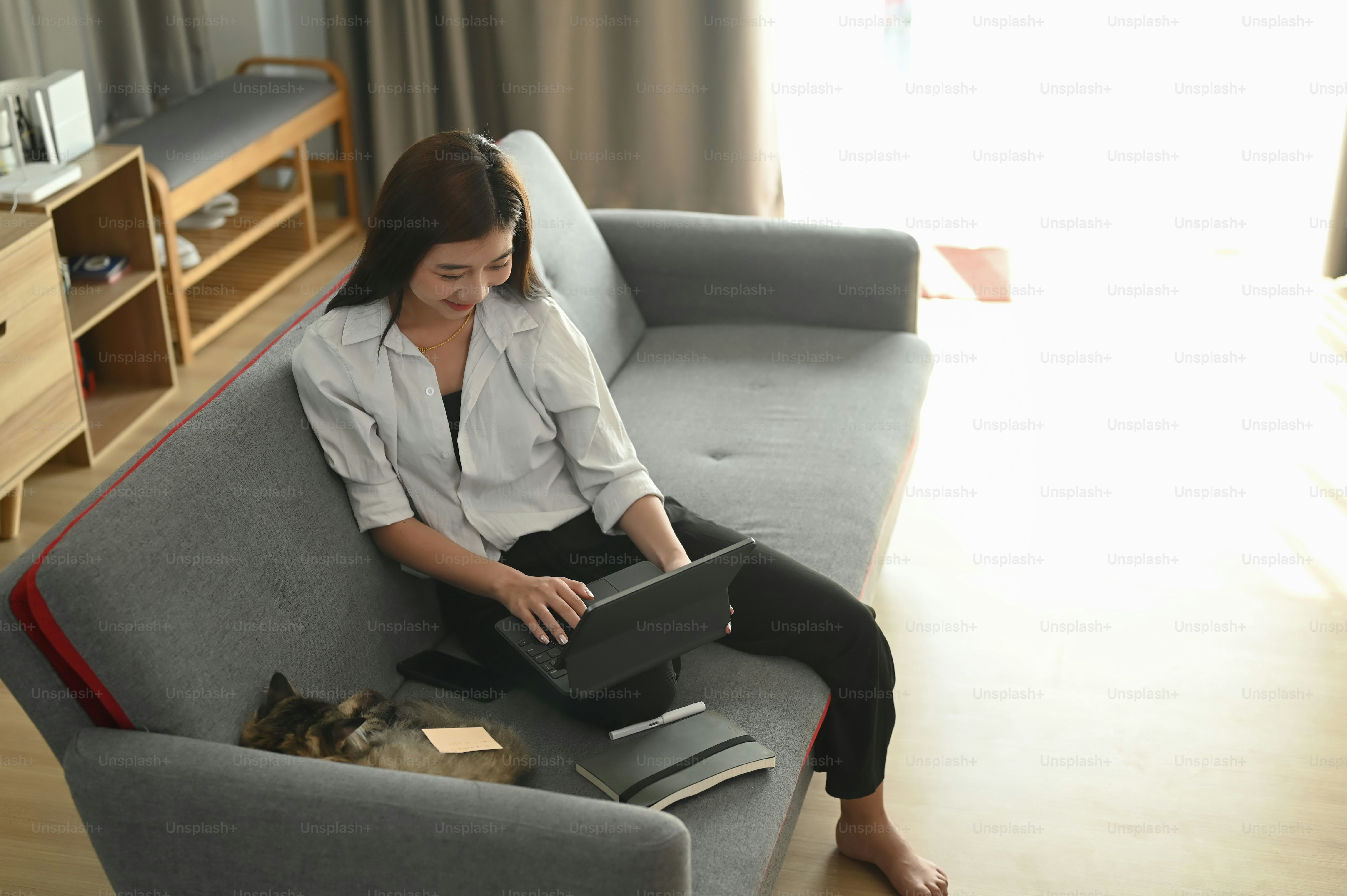 A cheerful young woman enjoys surfing the web with a computer tablet while sitting on couch at home.
