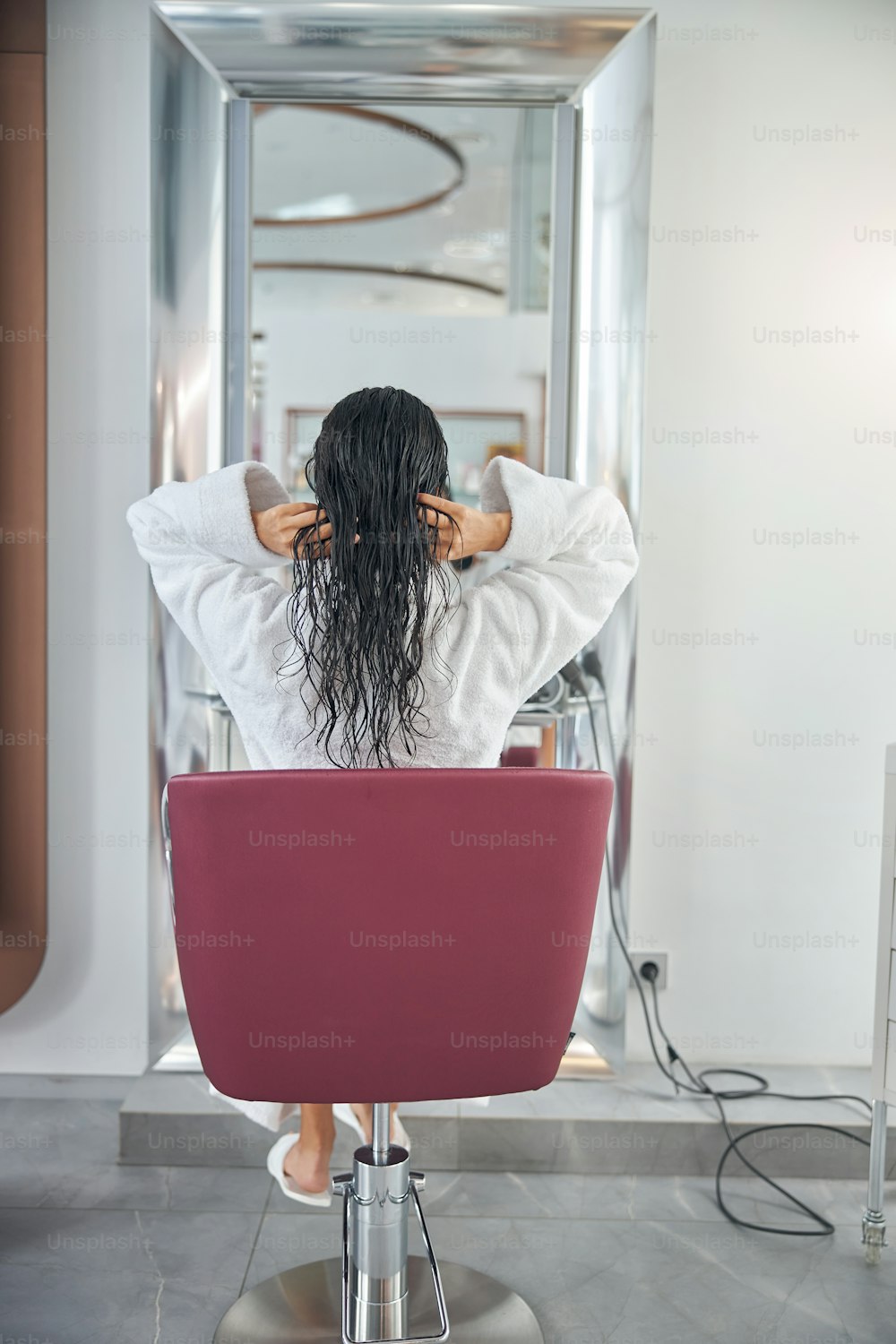 Back view of woman sitting in a chair in a beauty salon and touching wet hair