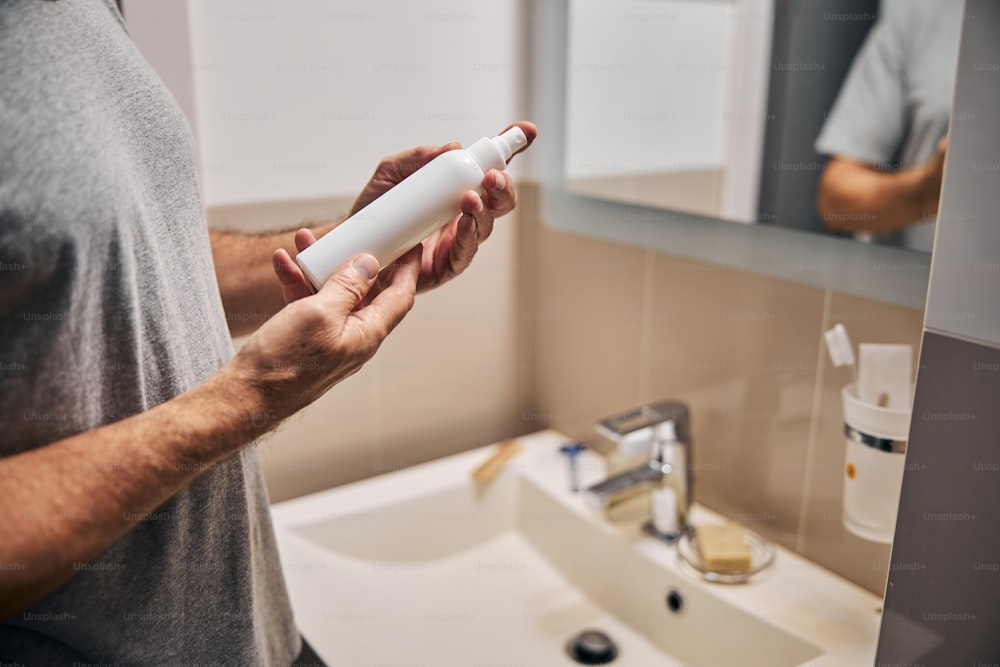 Cropped photo of man hands holding a bottle of cosmetic product near a sink