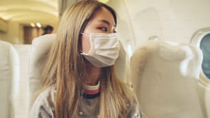 Traveler wearing face mask while traveling on commercial airplane . Concept of coronavirus disease or COVID 19 pandemic outbreak effects on tourism and airline business .