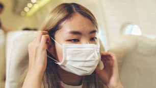 Traveler wearing face mask while traveling on commercial airplane . Concept of coronavirus disease or COVID 19 pandemic outbreak effects on tourism and airline business .