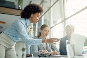 Black businesswoman and her female coworkers cooperating while working on a computer during the meeting.