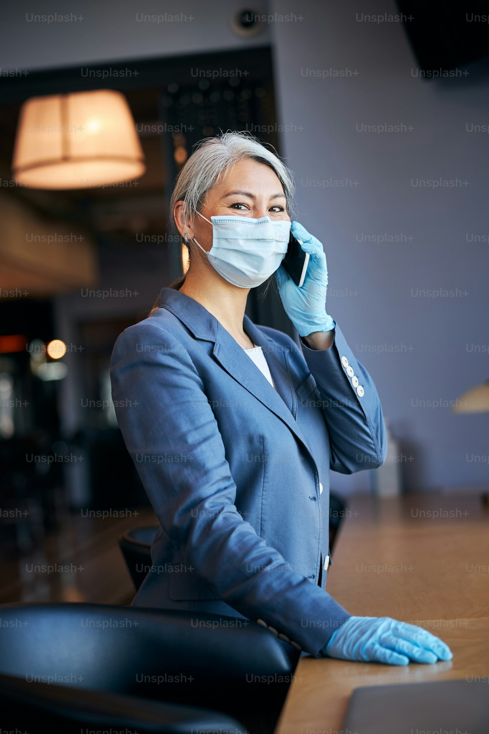 Elegant businesswoman wearing protective face mask and sterile gloves while having phone conversation at business center