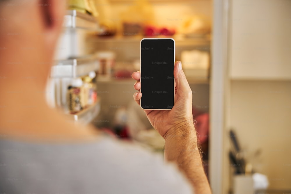 Copy-space photo of a hand with a smartphone with an open fridge in the background