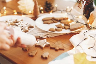 Decorare i biscotti di pan di zenzero con la glassa sul tavolo rustico. Tradizione delle vacanze di Natale e Avvento. Mani che decorano biscotti di Natale cotti con glassa di zucchero. Tempo per la famiglia