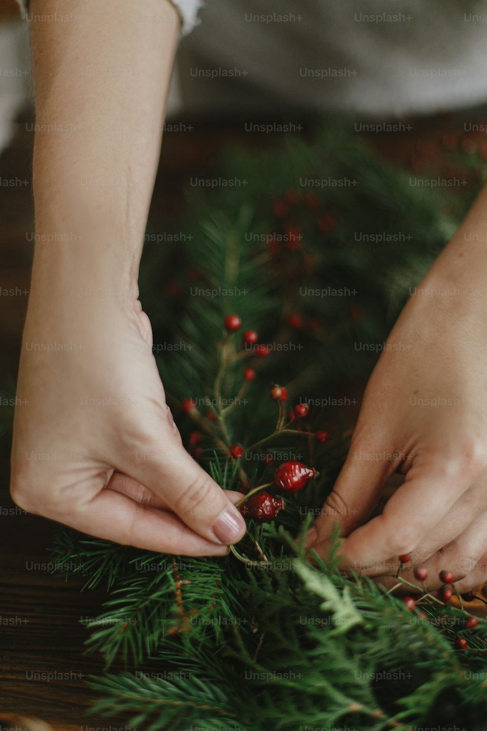 Florist hands holding berries and making rustic christmas wreath on wooden table with natural festive decorations. Seasonal winter workshop, holiday advent