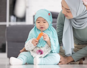 Muslimische Mutter im Hijab ist ihre kleine Tochter, die im Wohnzimmer sitzt, liebevolle Beziehung