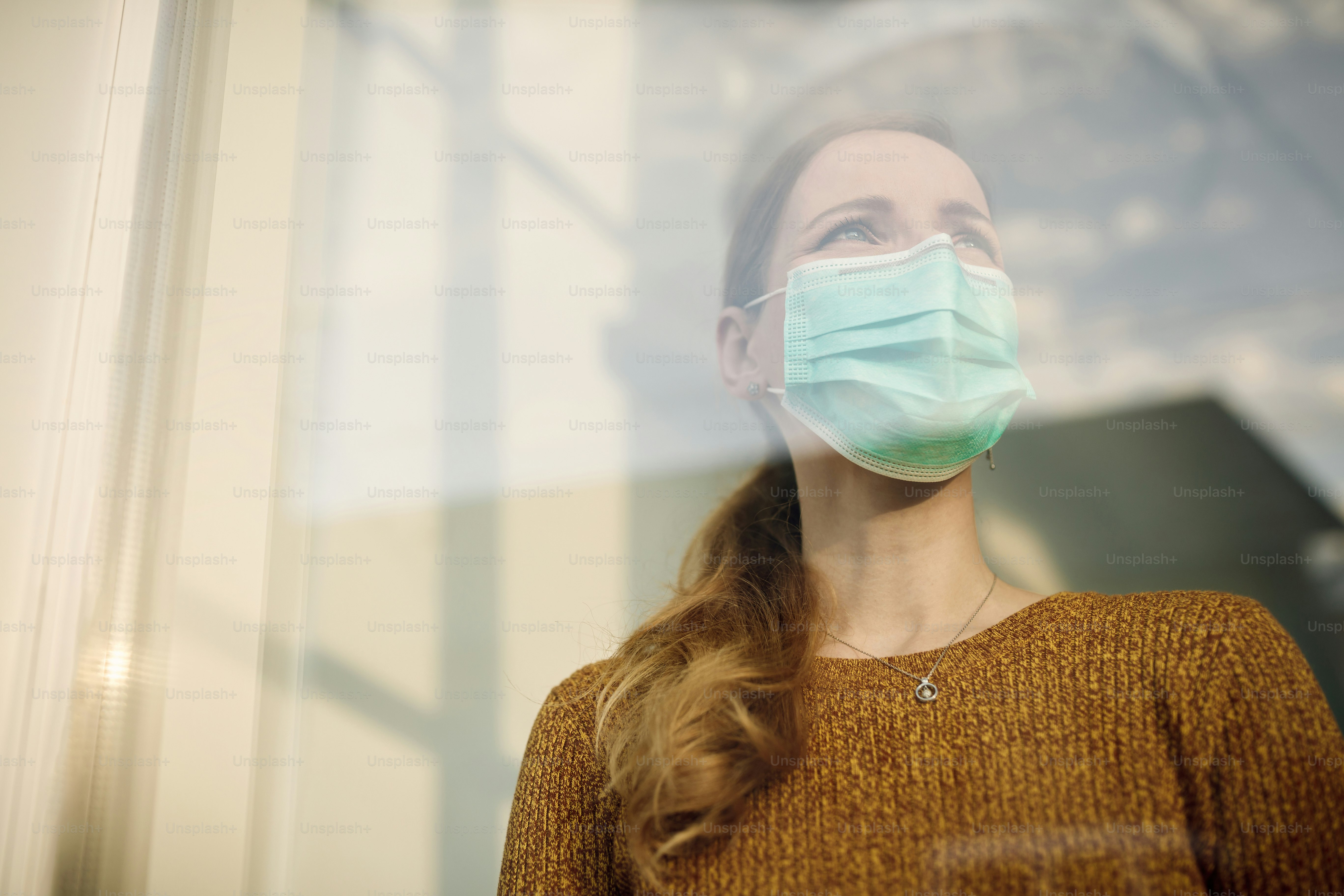 Vista de ángulo bajo de una mujer con máscara protectora y mirando a través de la ventana. Espacio de copia.