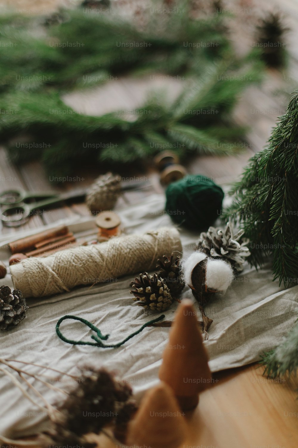 Fazendo grinalda de Natal rústica sobre mesa de madeira. Galhos verdes da árvore de Natal, pinhas, algodão, decorações festivas naturais, tesoura, barbante no fundo rústico. Workshop de férias