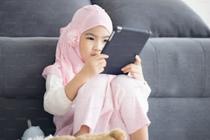 La chica musulmana está viendo vdo en línea a través de Internet en la tableta en la sala de estar por la mañana