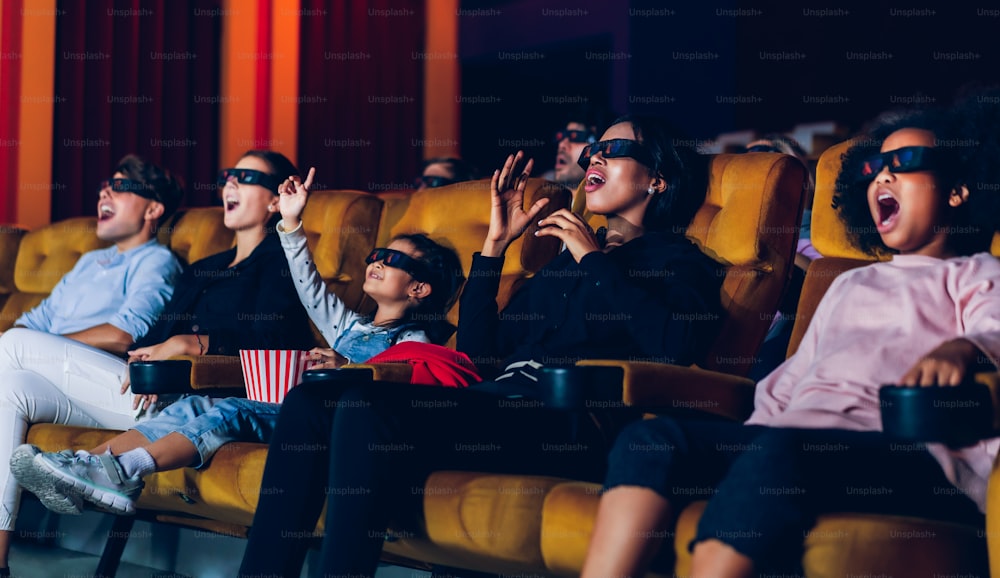 사람들의 그룹은 화면을 보고 흥미를 가지고 영화관에서 3D 안경으로 영화를 보고, 흥분하고 팝콘을 먹습니다.