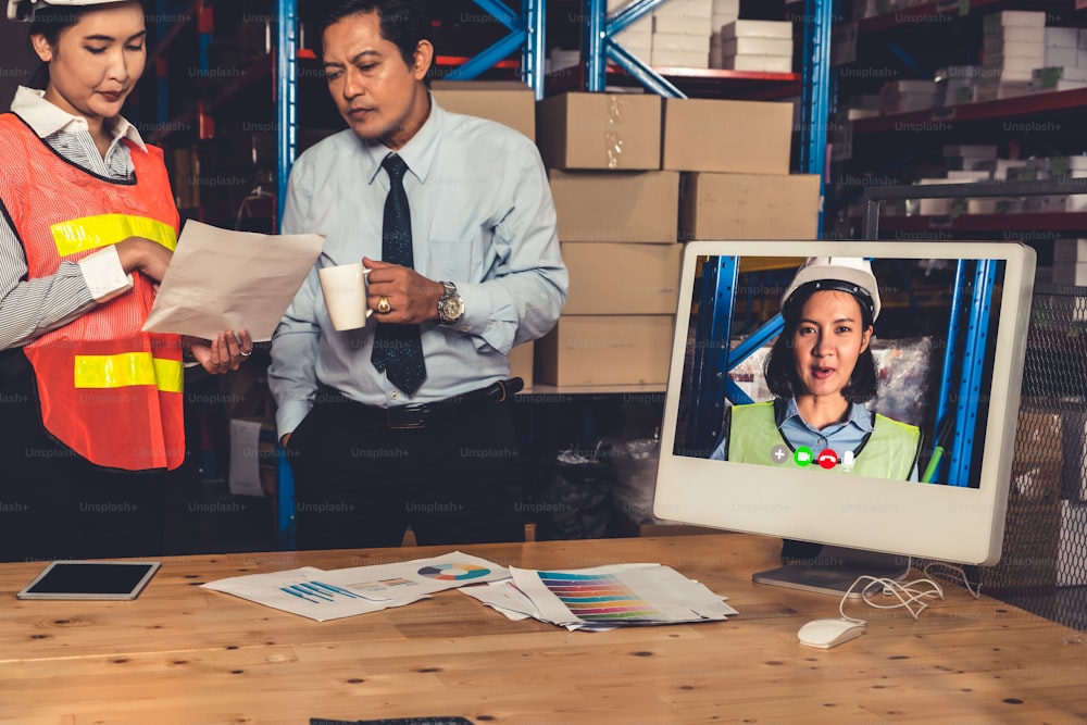 Warehouse staff talking on video call at computer screen in storage warehouse . Online software technology connects people working in logistic factory by virtual conference call on internet network .