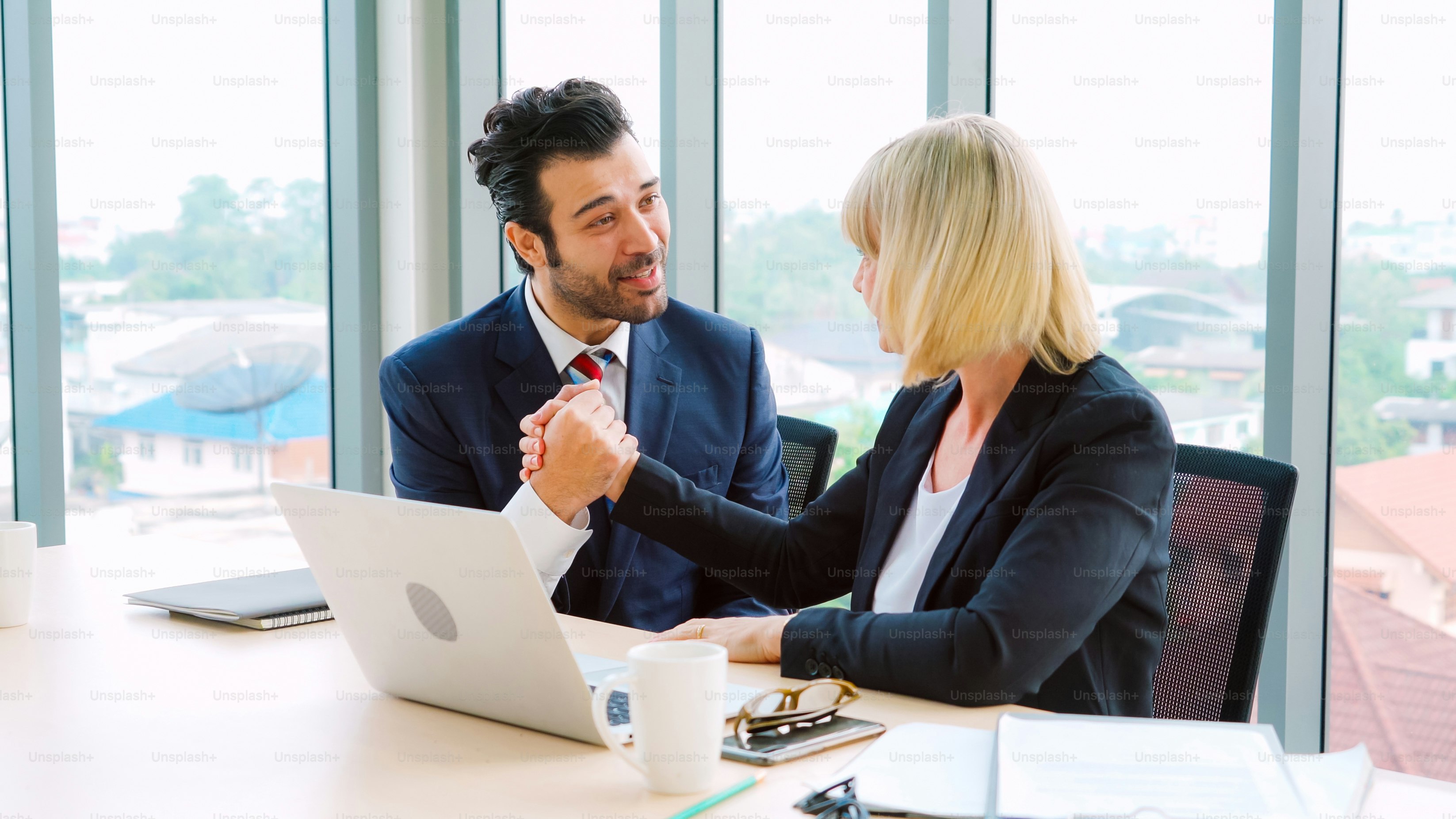 Two happy business people celebrate at office meeting room. Successful businessman congratulate project success with colleague at modern workplace while having conversation on financial data report.