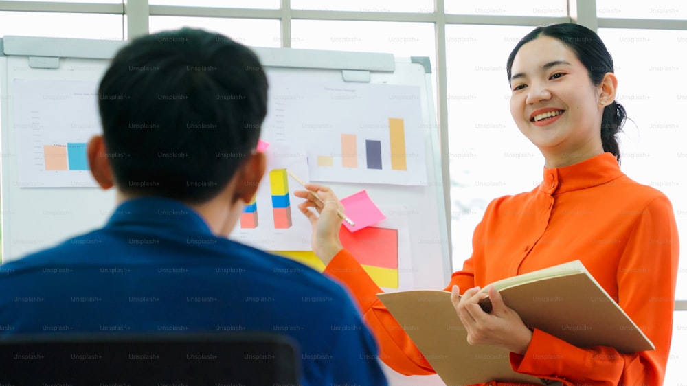 Young woman explains business data on white board in casual office room . The confident Asian businesswoman reports information progress of a business project to partner to determine market strategy .