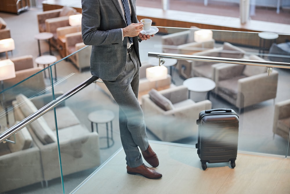 Beschnittenes Foto eines Reisenden, der sein Gepäck bewacht, während er auf einer Treppe einen Kaffee trinkt