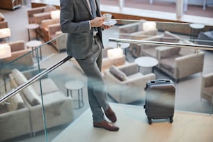Beschnittenes Foto eines Reisenden, der sein Gepäck bewacht, während er auf einer Treppe einen Kaffee trinkt
