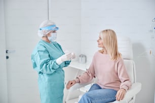 Experienced lab technician in sterile gloves and a face shield staring at a blonde lady
