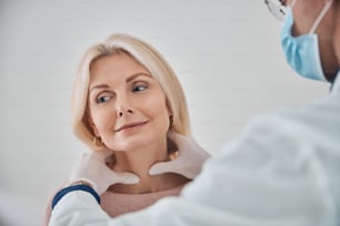 Profesional de la salud con mascarilla y guantes estériles palpando la glándula tiroides de la paciente femenina