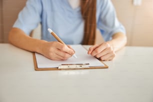 Cropped photo of a young lady in doctor uniform siitting at the table and writing on paper sheet