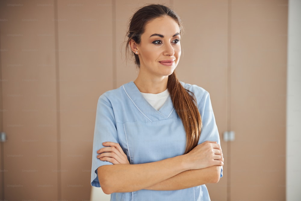 Waist-up photo of a beautiful lady wearing nurse scrubs and having her arms crossed on chest