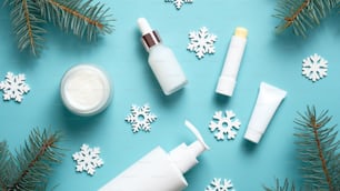 Set of winter skincare cosmetics on blue background. Packaging design template. Moisturizer cream jar, lipstick, pump bottle, tube, snowflakes and fir tree branches. Flat lay, top view.