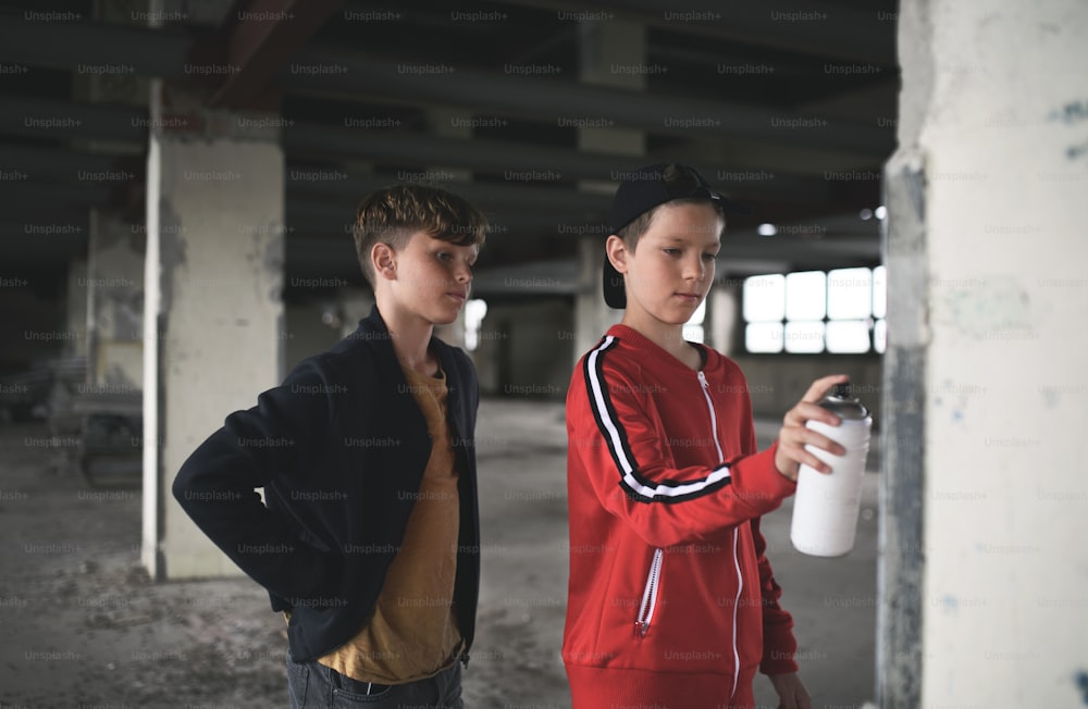 Gruppe von Teenagern Jungenbande steht drinnen in verlassenen Gebäuden, mit Sprühfarbe an der Wand.