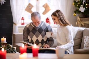Portrait of young woman with grandfather indoors at home at Christmas, looking at photo album.