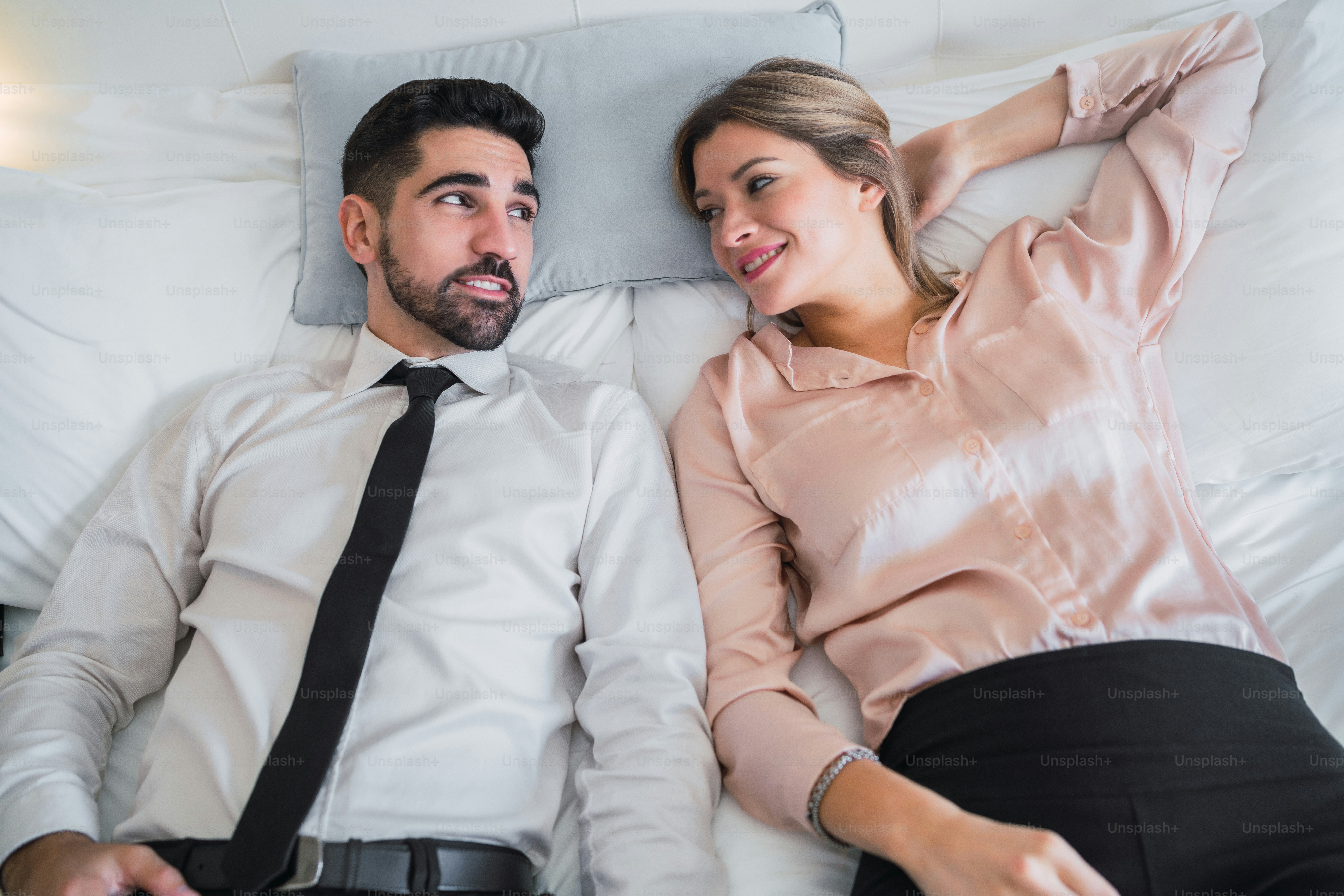 Portrait of two business people taking a break from work and laying on bed at the hotel room. Business travel concept.