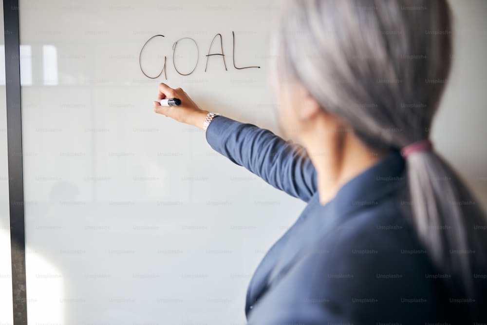 女性がオフィスで新しいプロジェクトに取り組んでいる間、ボード上の女性の手書きの単語の目標のクローズアップ