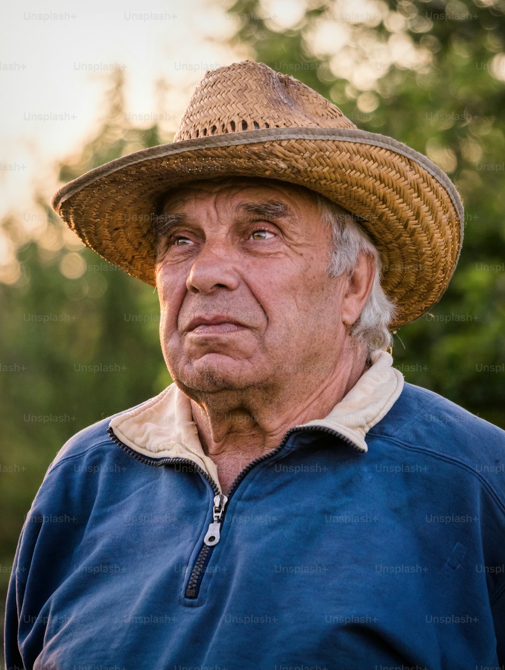 Buona vita da pensionato. Un uomo anziano con un cappello di paglia sullo sfondo di un giardino serale soleggiato. Giardinaggio per il tempo libero