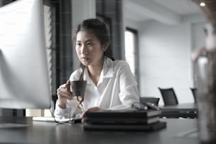 Businesswoman is watching online webinar with startup project on computer pc while drinking coffee at office.
