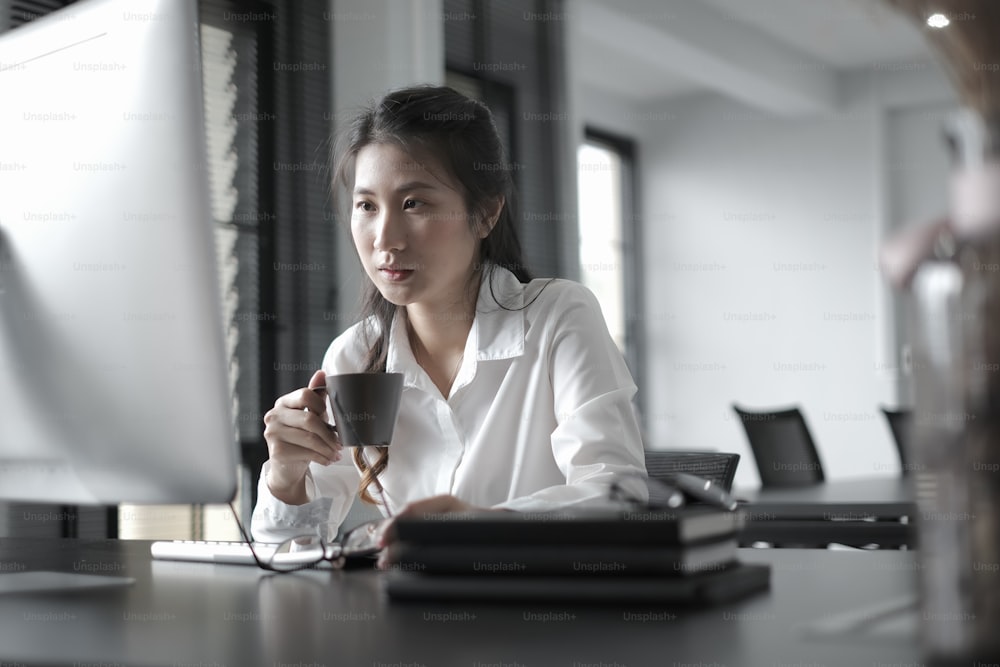 Geschäftsfrau schaut Online-Webinar mit Startup-Projekt auf Computer-PC, während Kaffee im Büro trinken.
