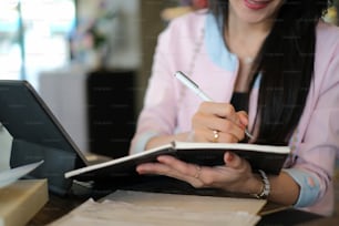 La foto recortada de la mujer de negocios está escribiendo información en el bloc de notas.