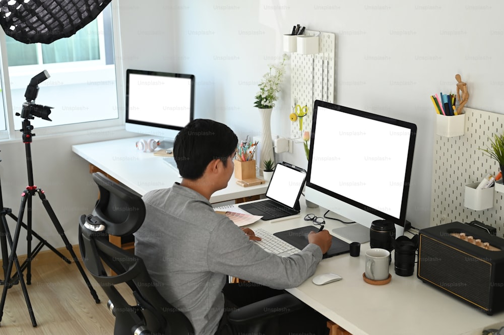 Graphic designer or photographer is working with empty screen computer and digital tablet at his workspace.