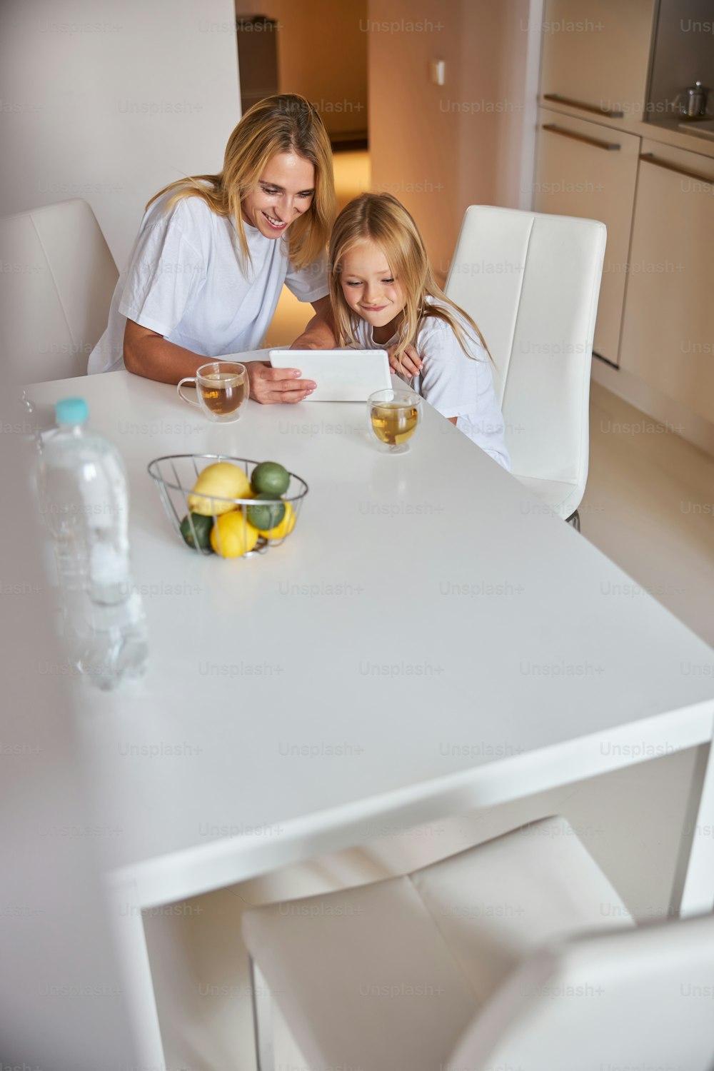 Nahaufnahme Porträt einer glücklich lächelnden Frau und eines kleinen Mädchens, das auf den Bildschirm schaut modernes Tablet, während sie Zeit in der heimischen Küche verbringen