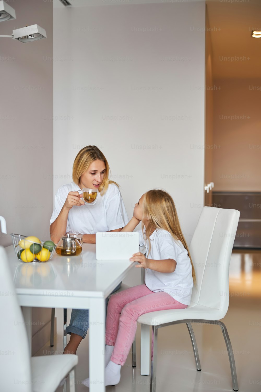 Full length portrait of young nanny spending time with little female child while having conversation in the room inside