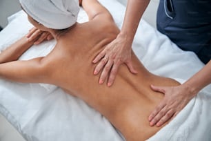 Close up of female with towel on her head lying on massage table while receiving professional back massage