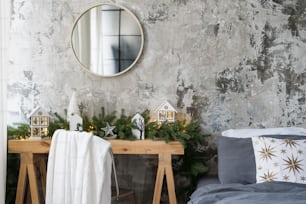 Elemento della camera da letto in un appartamento dal design moderno con interno soppalcato, letto morbido e confortevole, specchio sopra l'arredamento della stagione invernale su tavolo in legno vicino al muro rustico