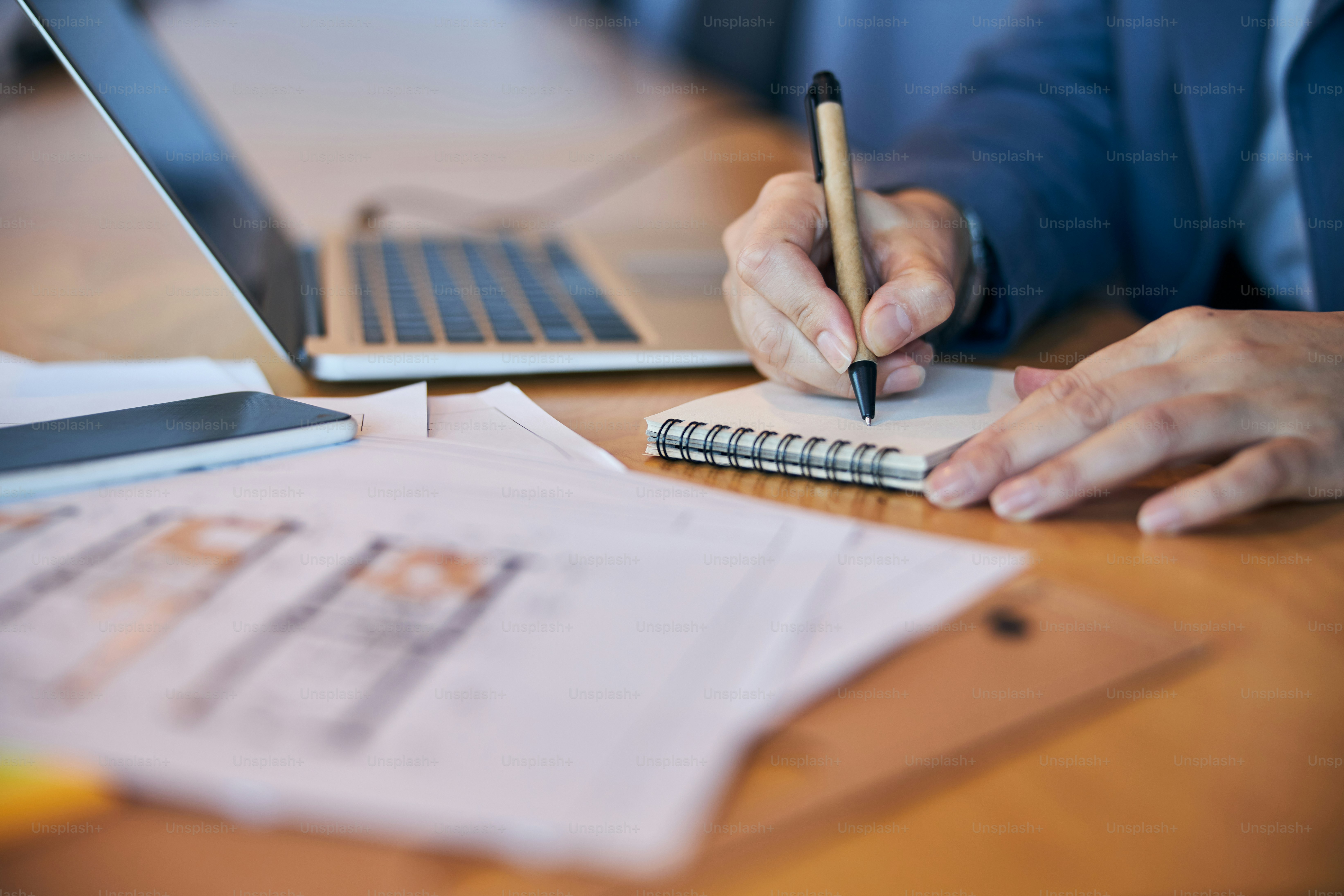 Close up of woman making notes while sitting at the table with laptop, smartphone and papers