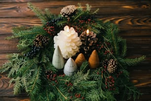 Buon Natale! Ghirlanda moderna fatta a mano con alberelli, candele e pigne su tavolo rustico in legno, tavola di Natale. Decorazioni festive ed eleganti per la cena delle vacanze a casa.