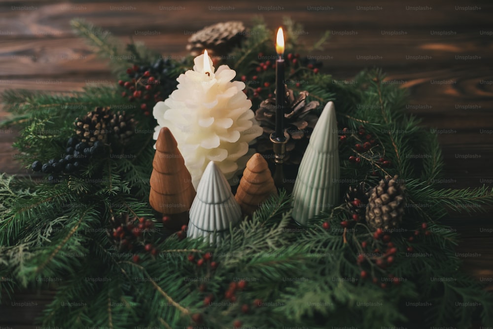 Weihnachtstischdekoration, moderner handgefertigter Kranz, kleine Weihnachtsbäume und Kerzen auf rustikalem Holztisch. Festliche stilvolle Dekorationen für das Weihnachtsessen zu Hause. Frohe Weihnachten!