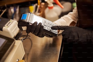 Close up hands in rubber gloves holding a terminal for payments and pushing the buttons
